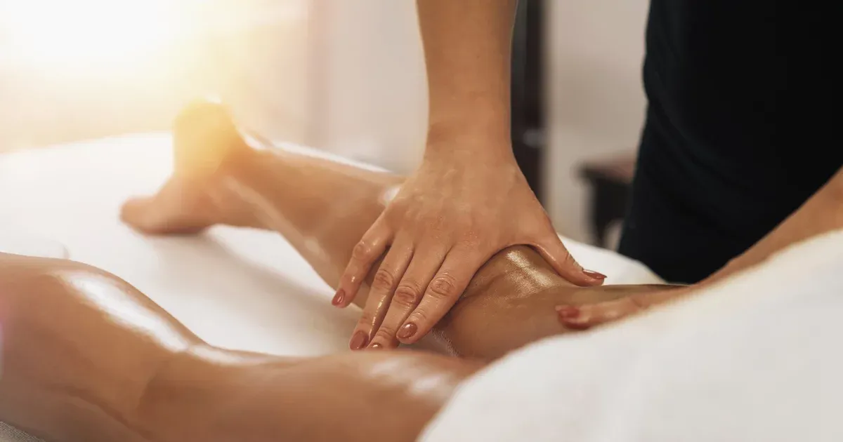 Hands massaging a leg covered in oil on a white surface.