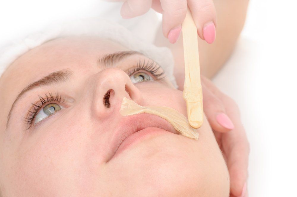 Woman having lip hair waxed; aesthetician applies wax with a wooden spatula.