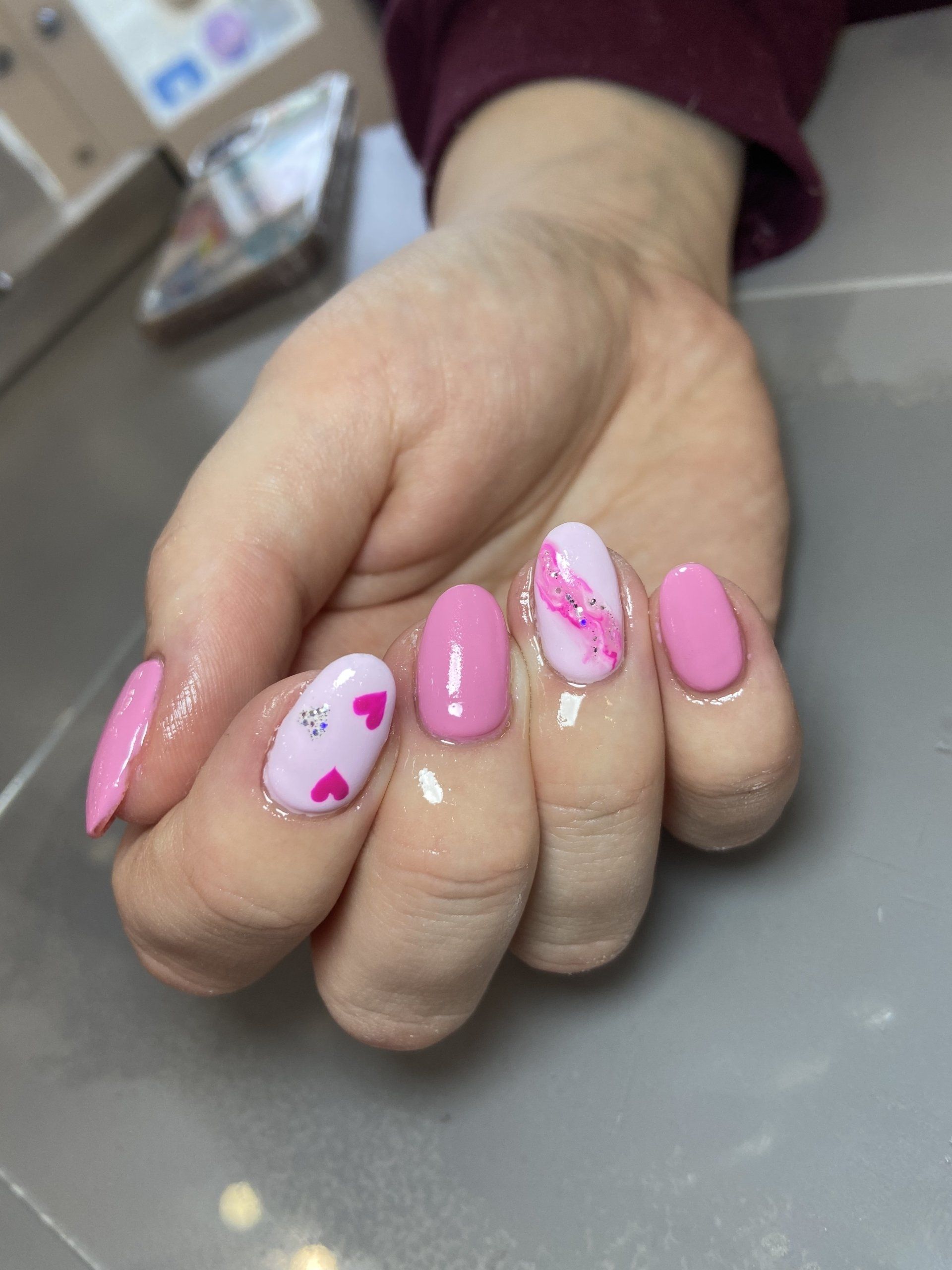 Pink oval nails with heart and marble designs.