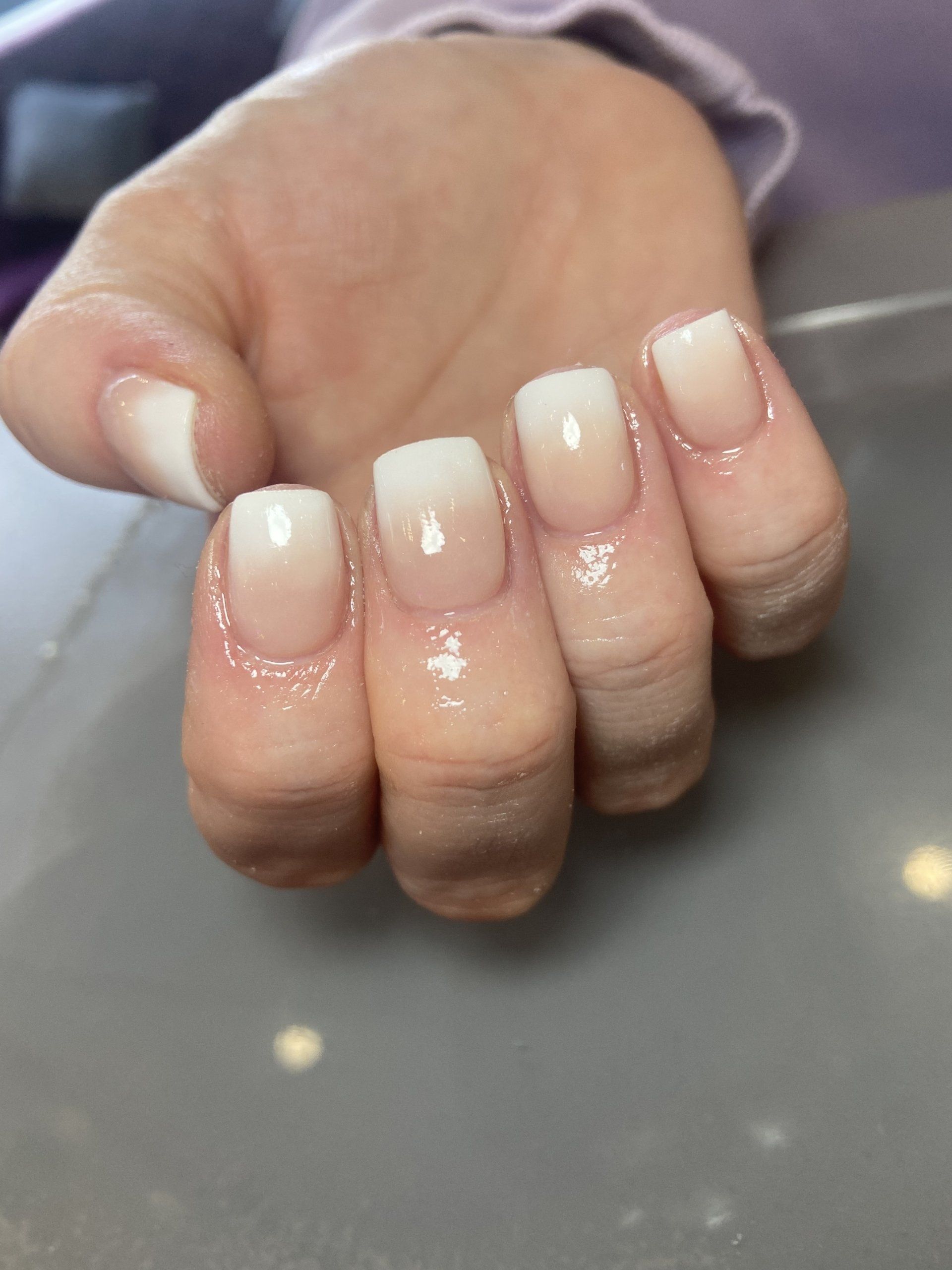 Hand with square, white-tipped ombre nails.