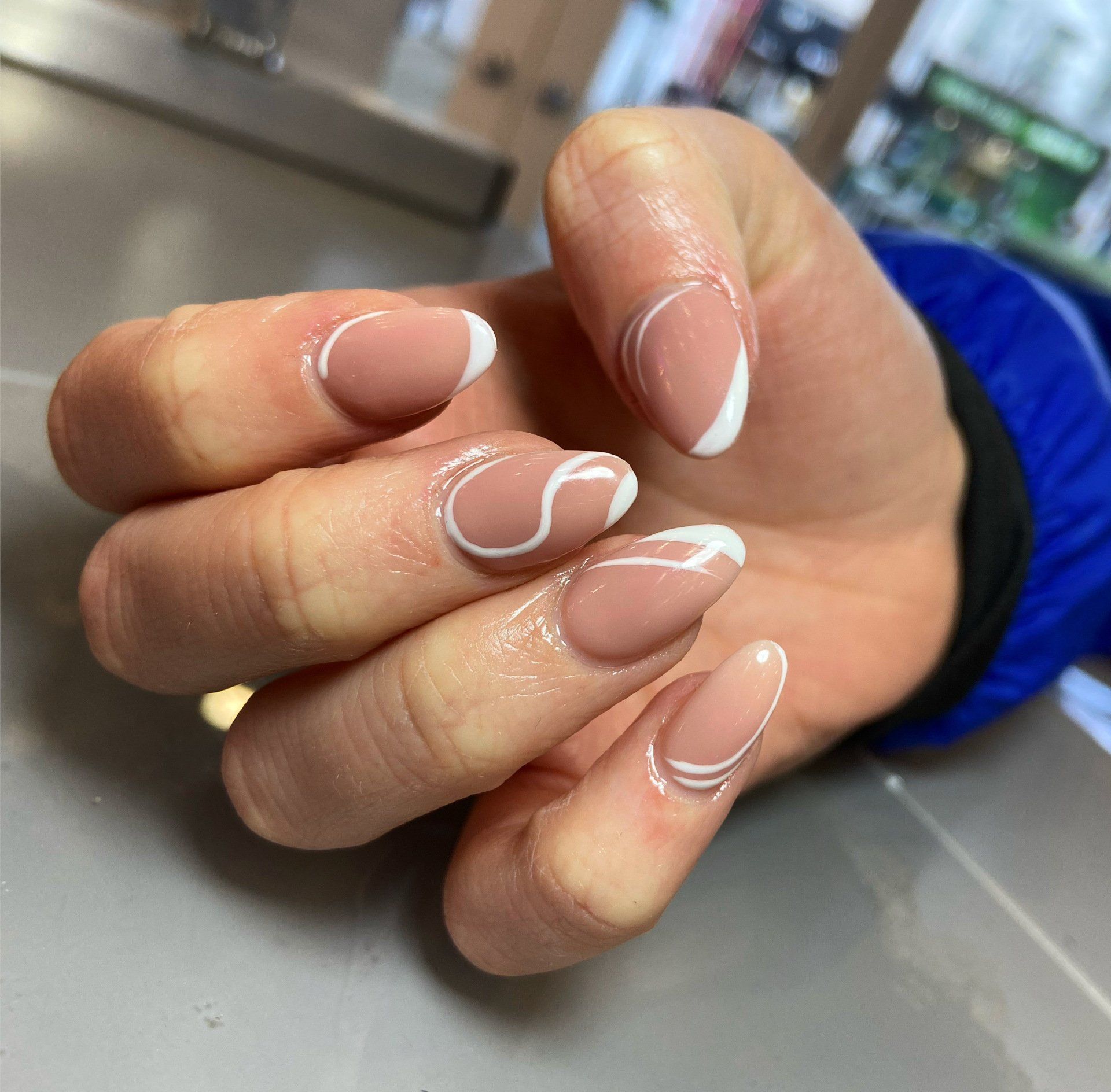 Hand with almond-shaped nails, nude base, white curved lines.