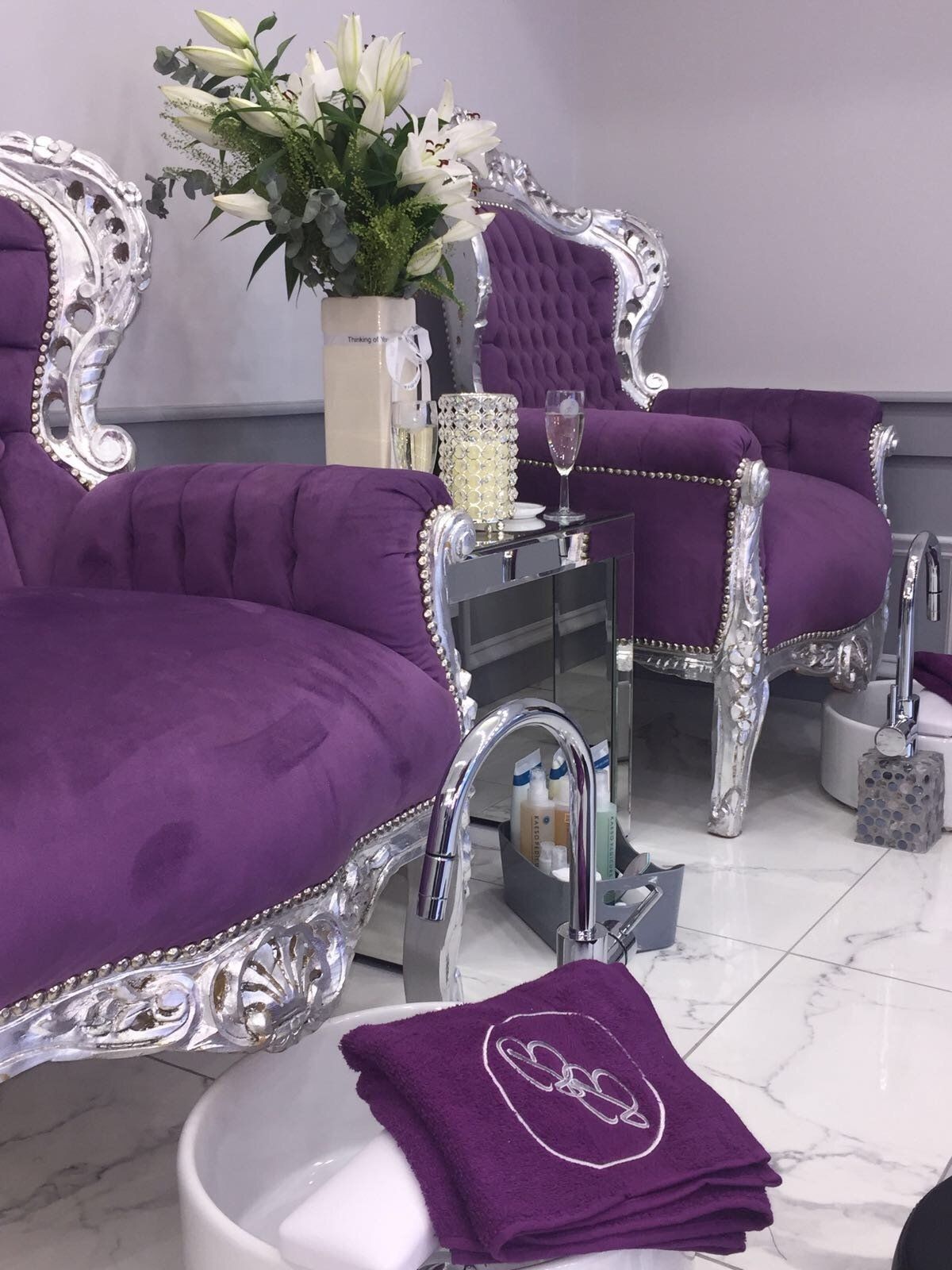 Purple pedicure chairs with silver trim, white flowers, and a towel in a salon setting.