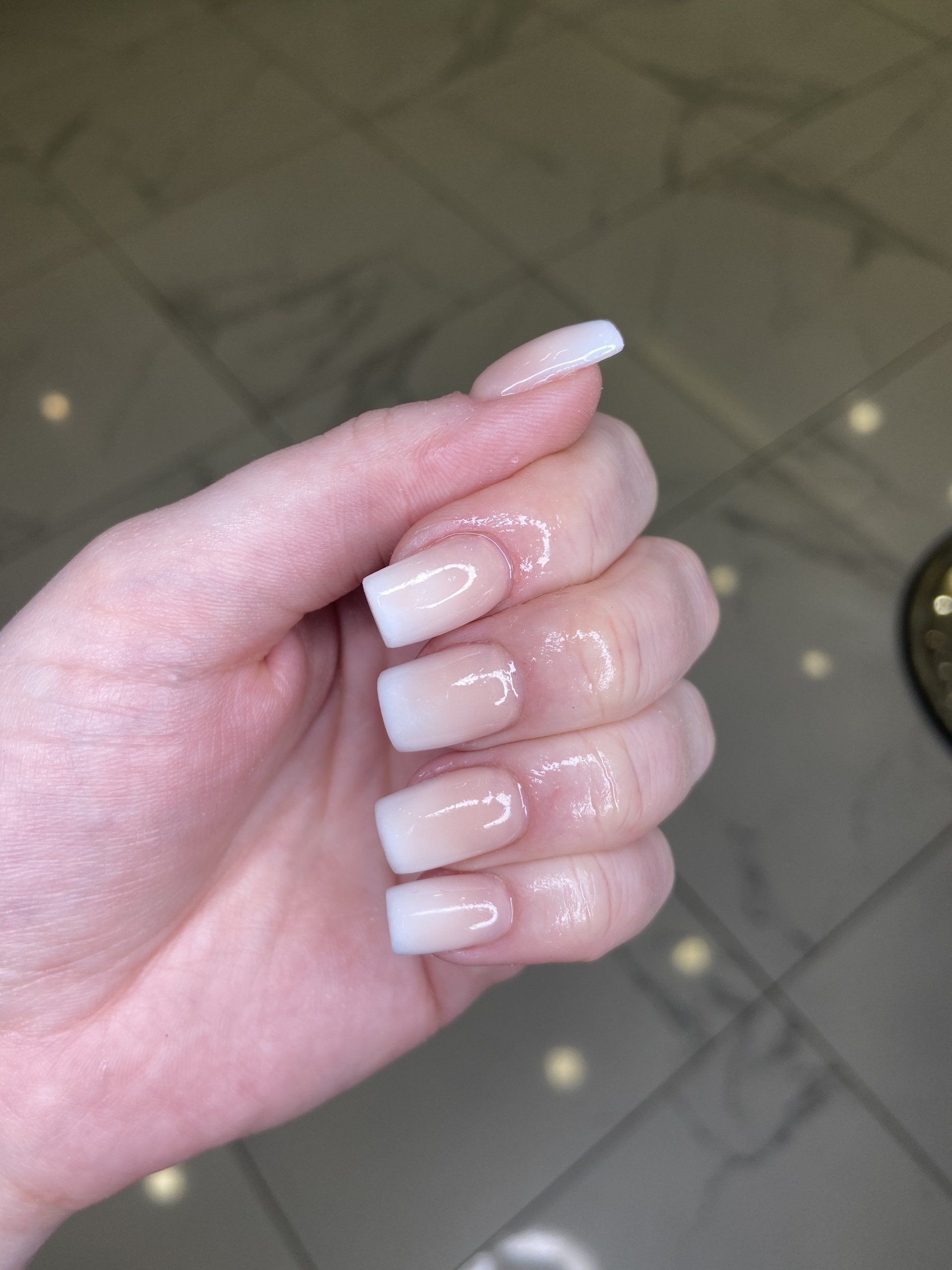 Hand with square-shaped nails in a white to nude ombre gradient.