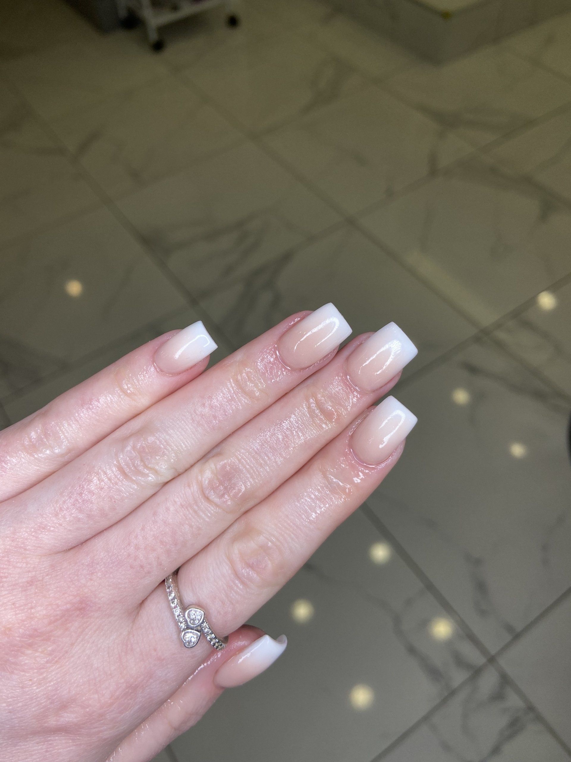 Hand with square French-tipped nails, wearing a diamond ring, indoors.