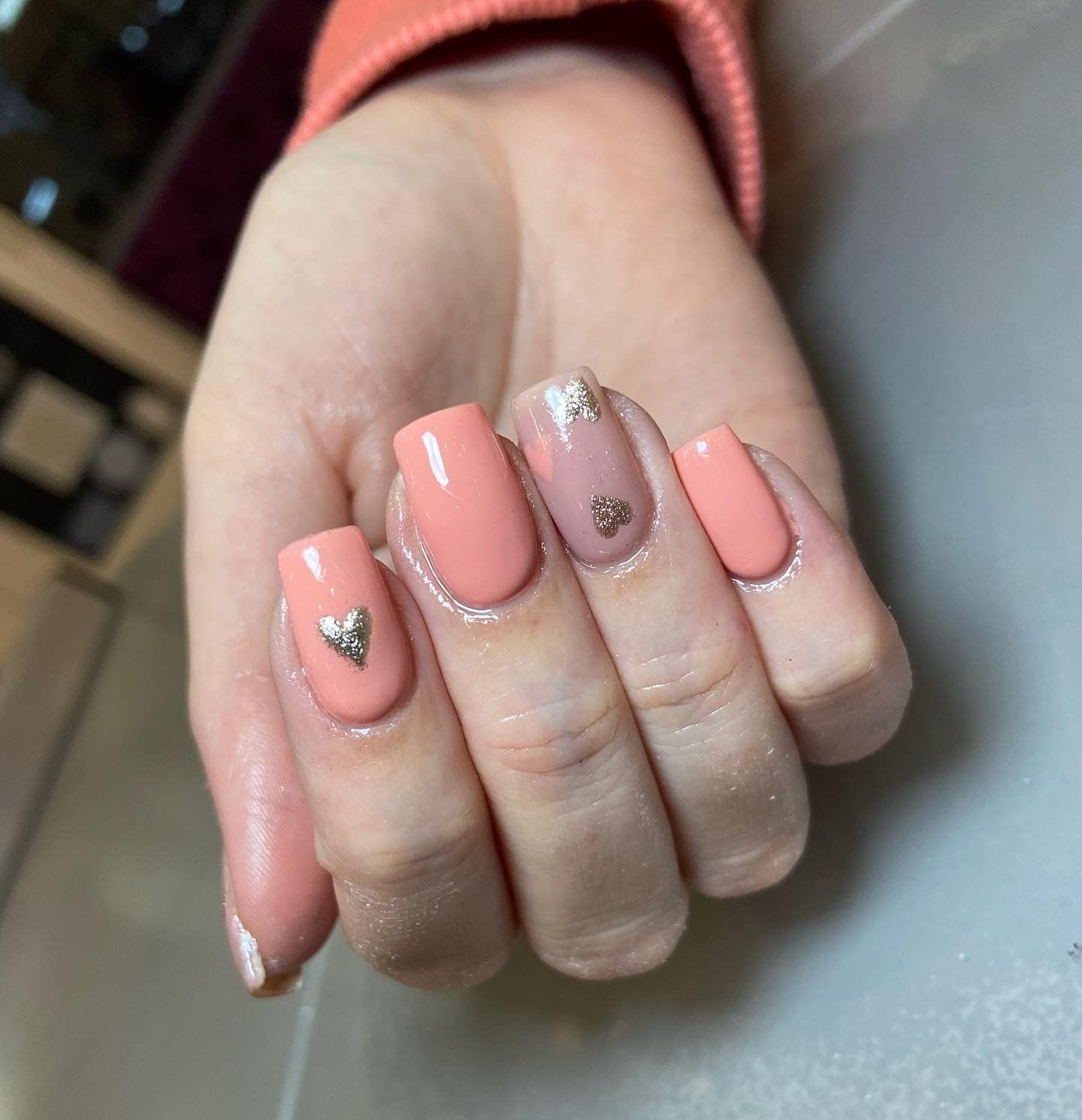 Hand with peach-colored nails; one accent nail with silver hearts.