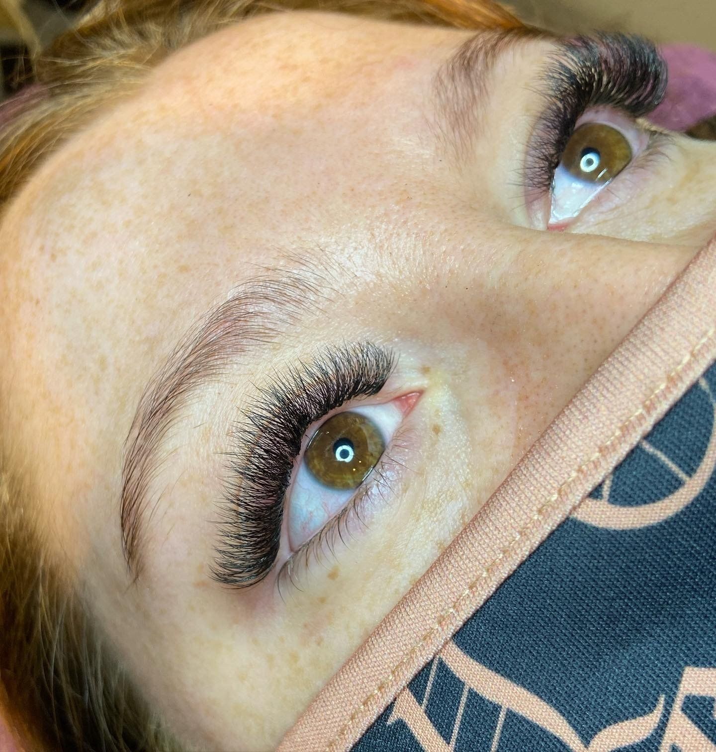 Close-up of a person with brown eyes, styled eyebrows, and full, dark eyelash extensions.