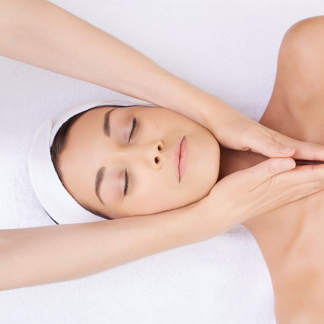 Woman receiving a spa treatment, with hands gently massaging her face and chest.