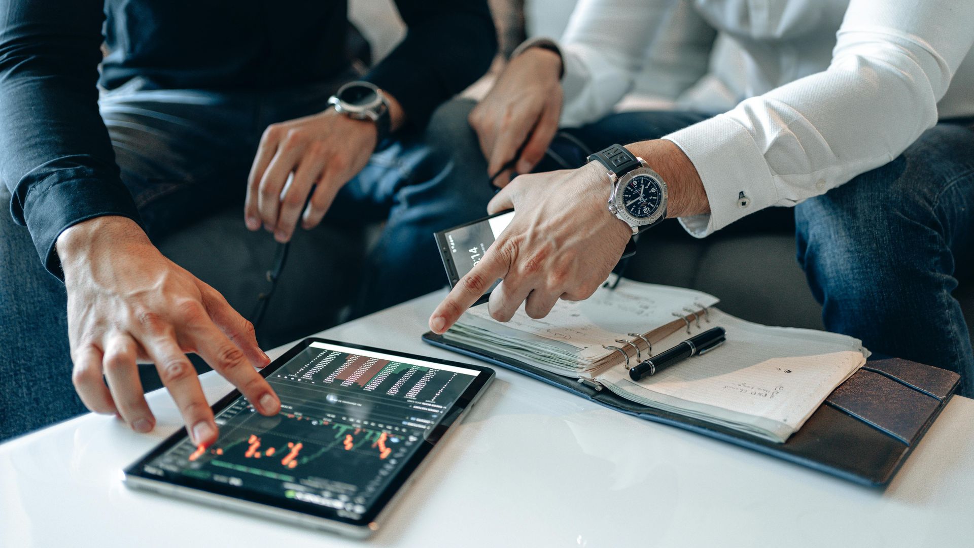 A man is sitting at a table with a laptop and shaking hands with a man.
