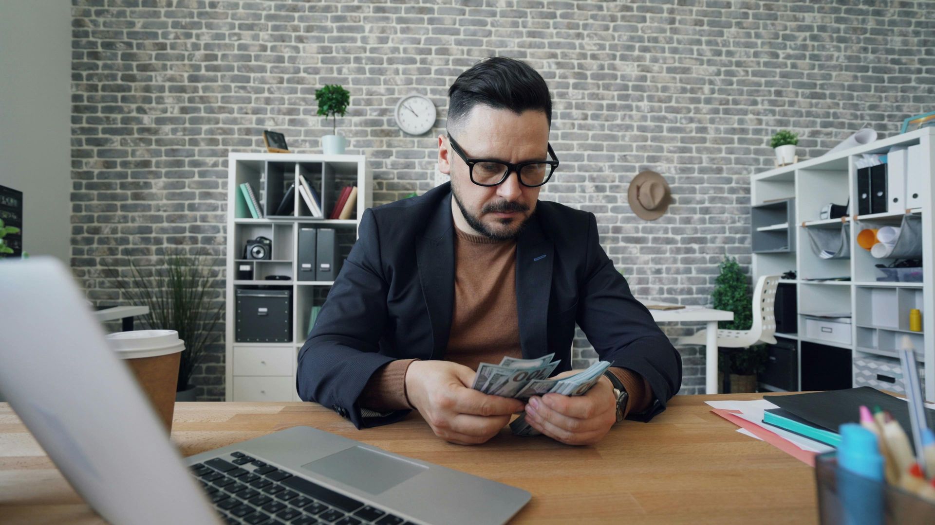 A man is sitting at a table with a laptop and shaking hands with a man.