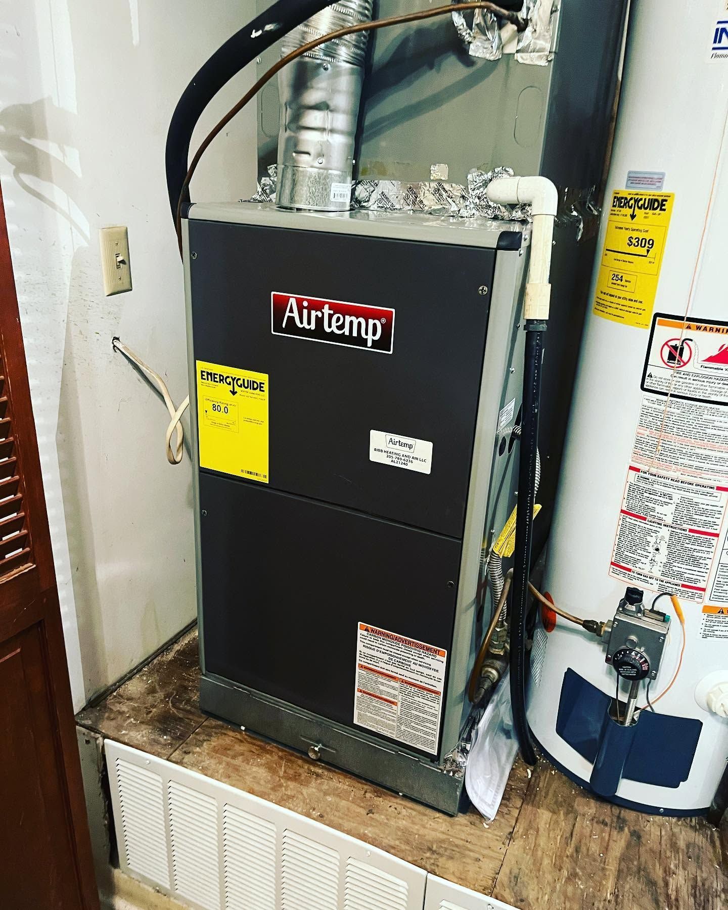 Black Airtemp furnace beside a white water heater in a utility closet.