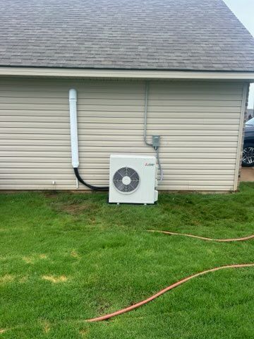 Outdoor air conditioning unit beside a beige house with white vent pipe and green lawn