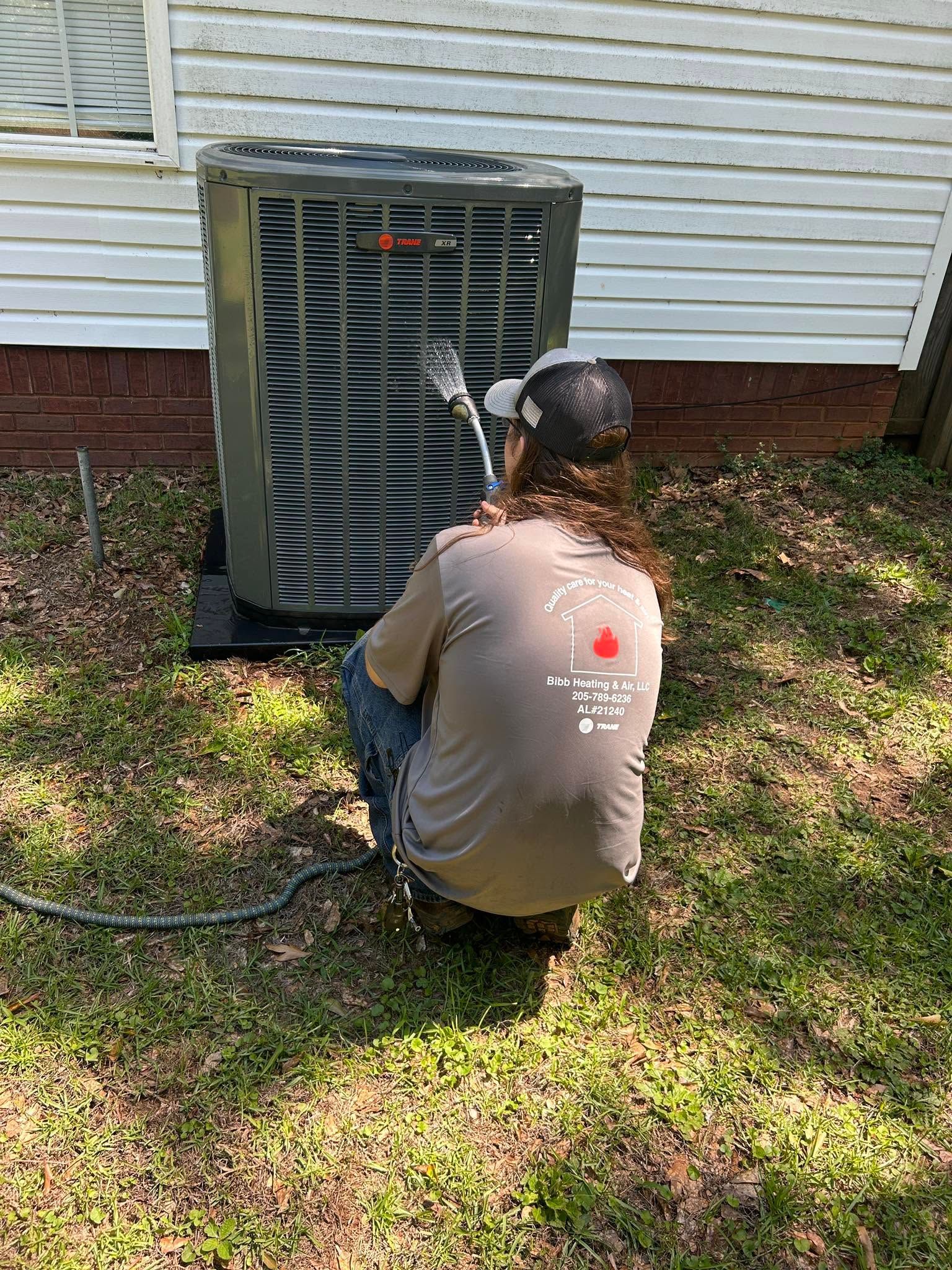 Technician kneeling by outdoor air conditioner unit, inspecting wiring beside a house.
