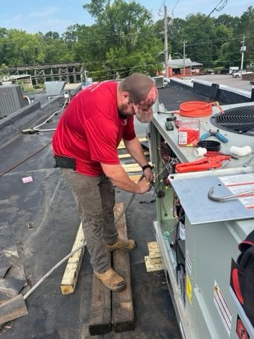 Worker in red shirt installing rooftop HVAC equipment on a flat roof.