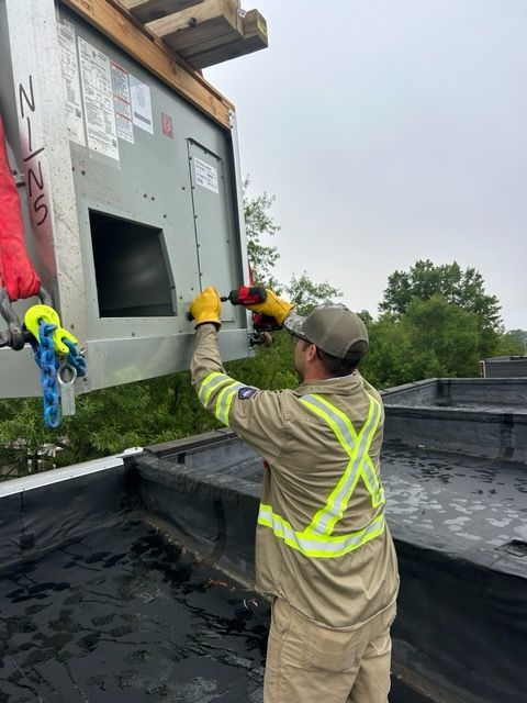 Worker in safety harness installing a vent on a building roof under overcast skies