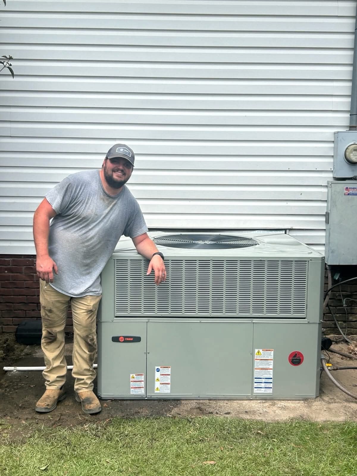 Man standing beside a gray outdoor HVAC unit against a white building wall.