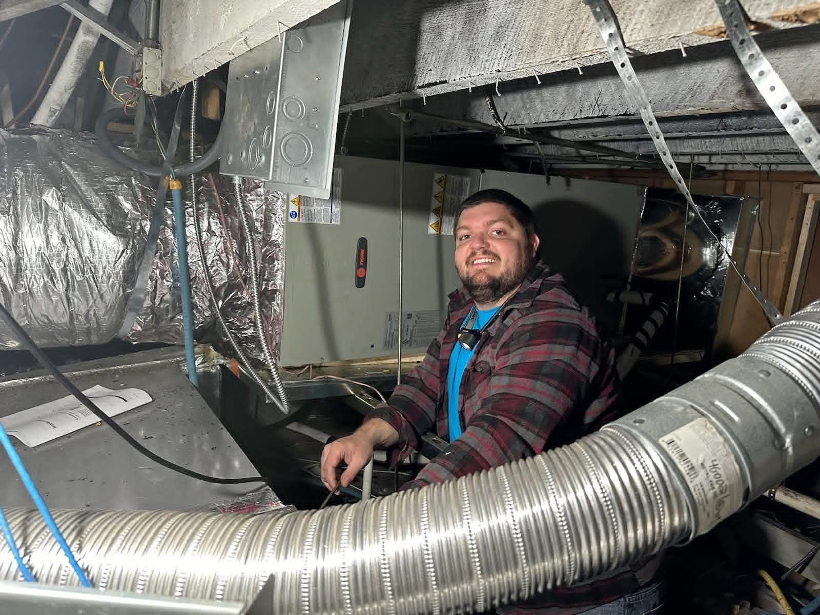 Person smiling inside an industrial crawlspace surrounded by ducts, cables, and equipment