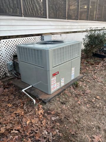 Gray outdoor HVAC unit beside a house with white lattice skirting and fallen leaves on the ground