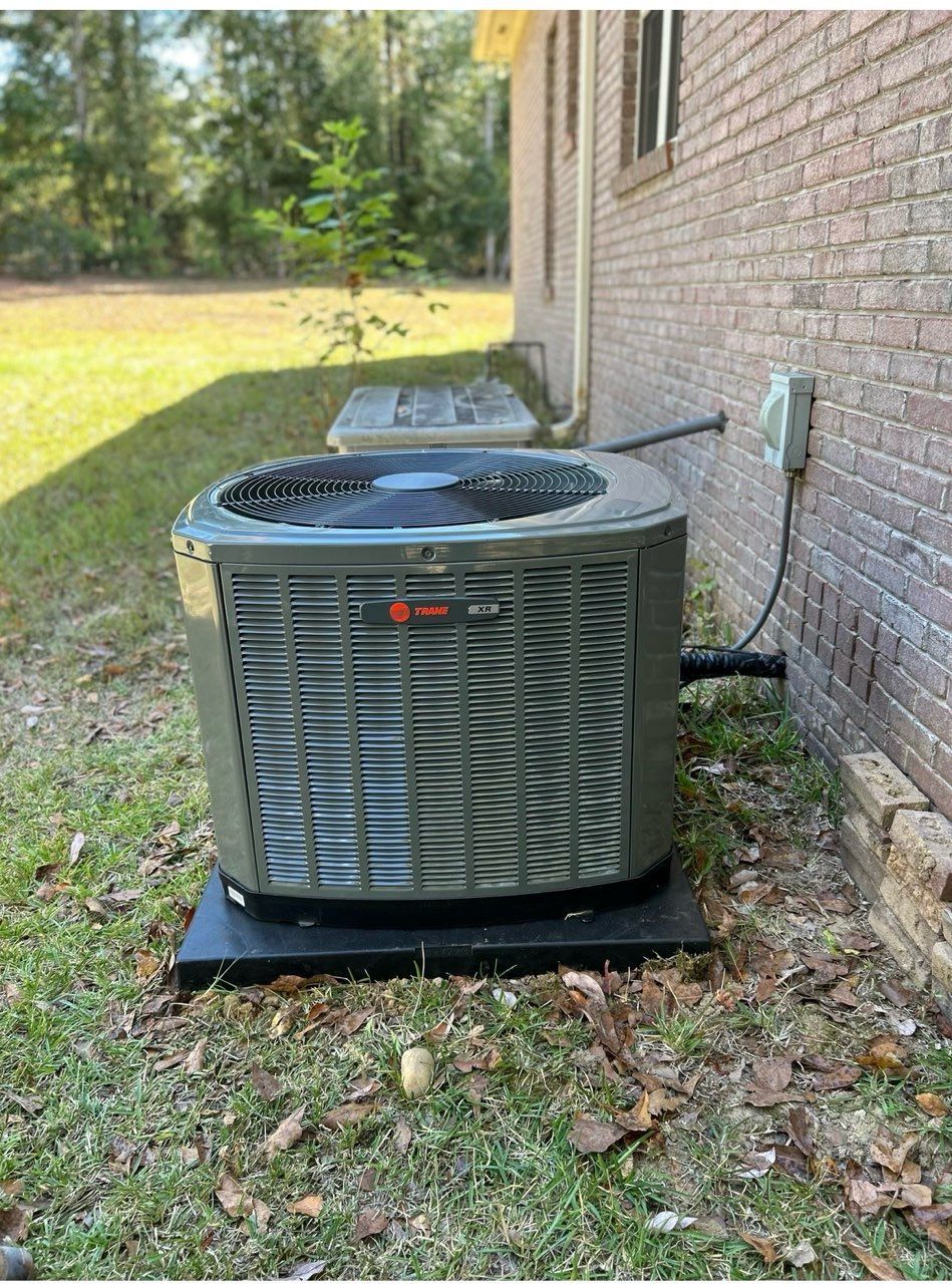 Outdoor HVAC condenser unit beside a brick house on a grassy lawn.