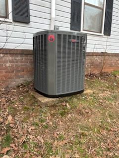 Gray outdoor air conditioner unit beside a brick foundation under house windows