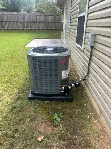 Outdoor central air conditioner unit beside a house with a fenced lawn.