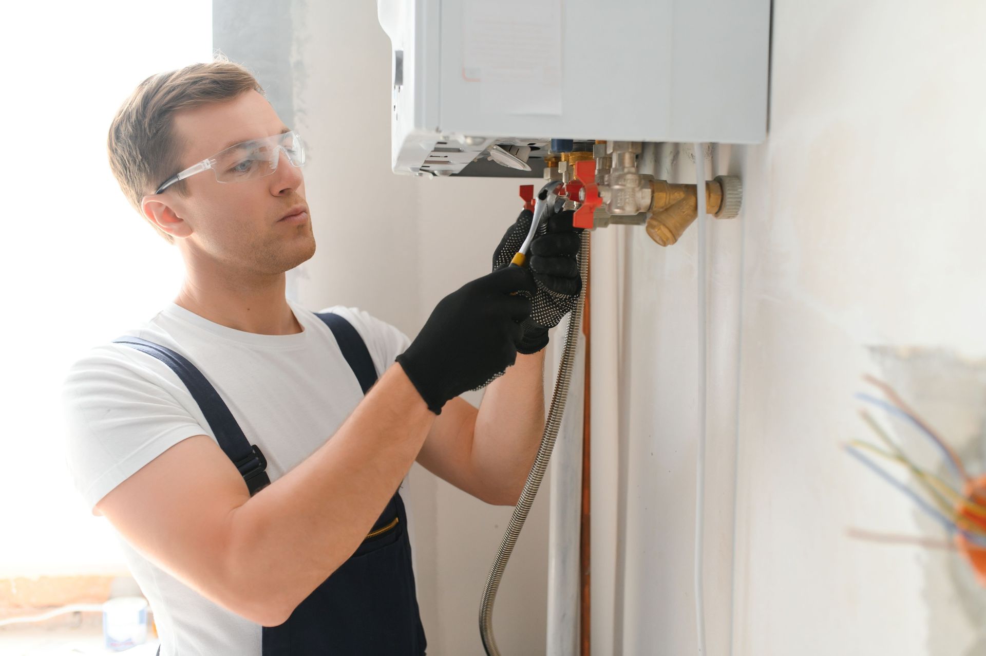 Technician repairing a wall-mounted boiler with tools, wearing safety glasses and gloves