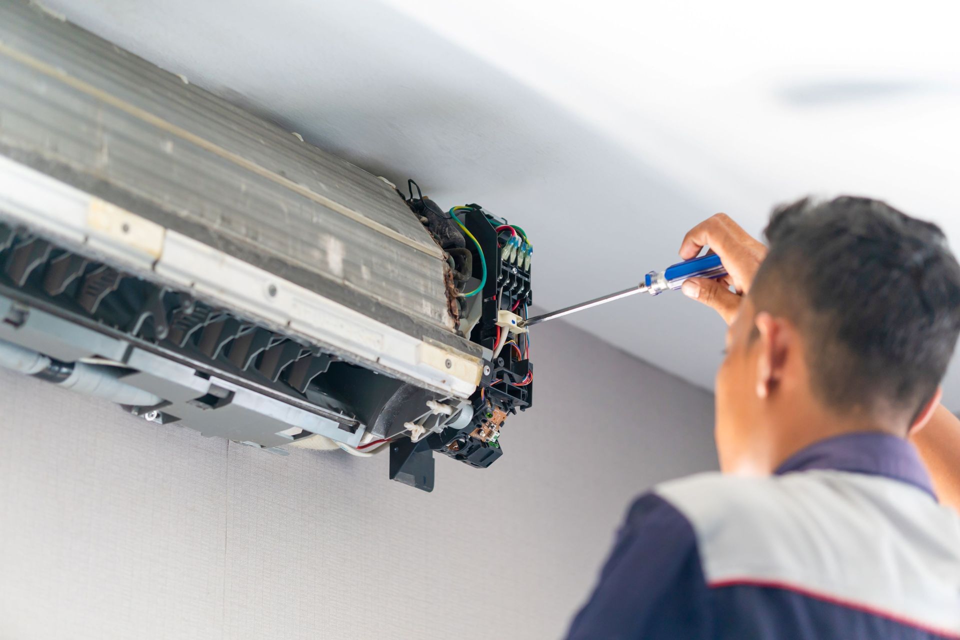 Technician repairing a wall-mounted air conditioner with a screwdriver