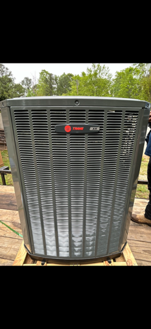 Gray Trane air conditioner condenser unit outdoors on a concrete pad, with trees in the background