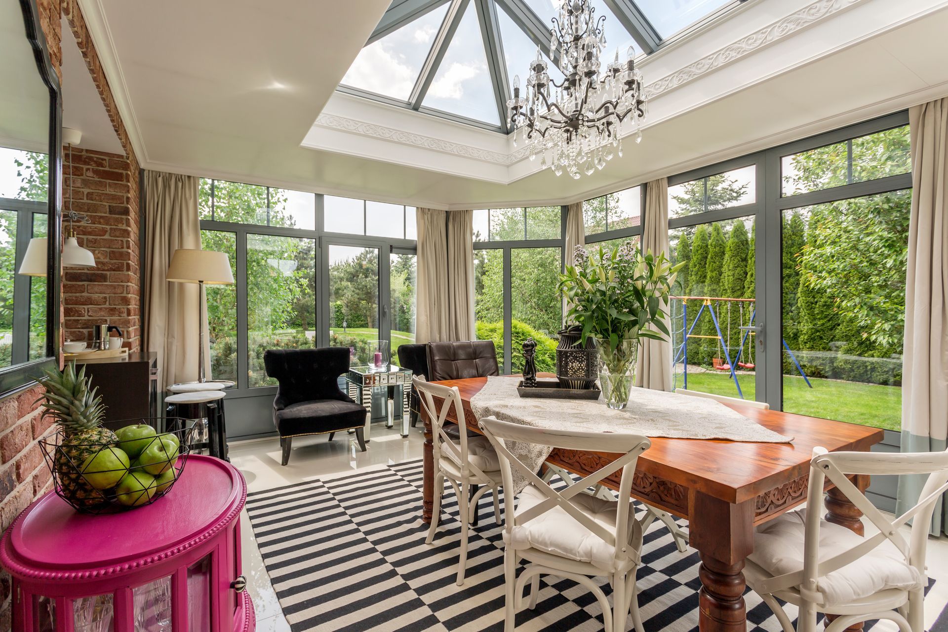 A cozy sunroom with large windows and skylights that are in need of Designer Solar Shades