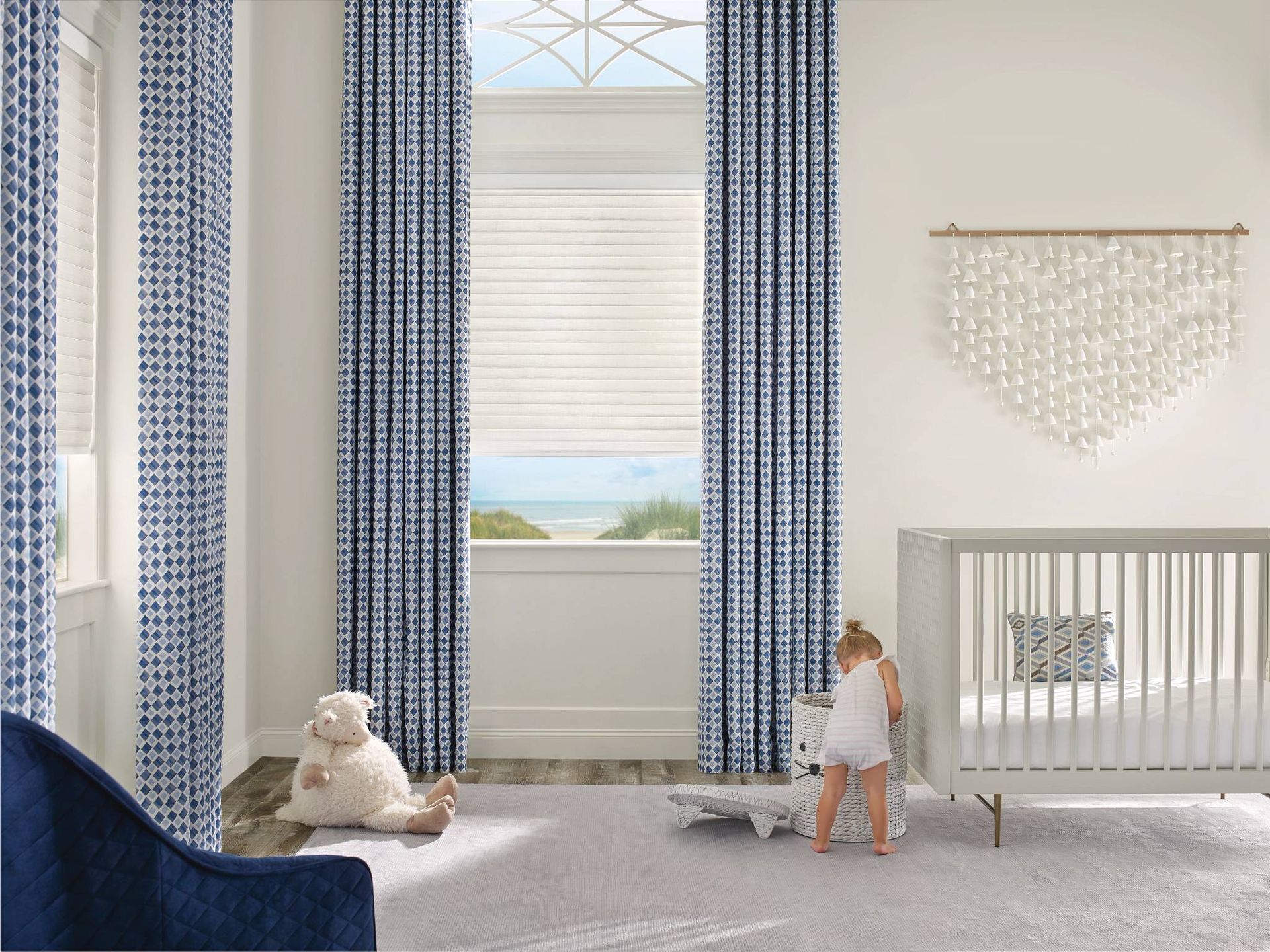 Sonnette® Roller Shades on tall windows in a white and blue nursery, layered with patterned drapes  at Window Magic Blinds & Drapery near Houston, TX
