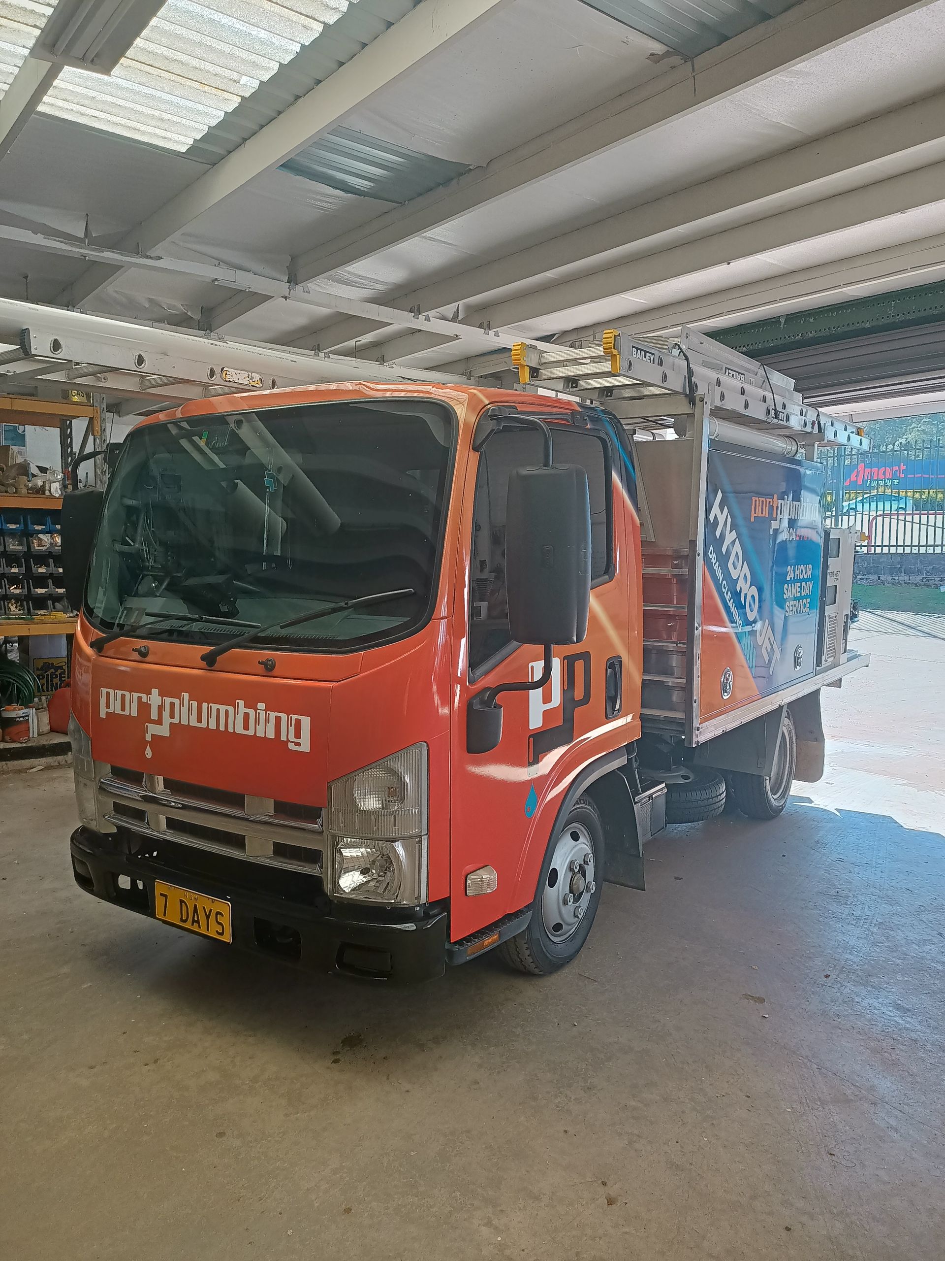 Orange Utility Truck Parked Inside a Covered Garage — Port Macquarie Plumbing In Port Macquarie, NSW