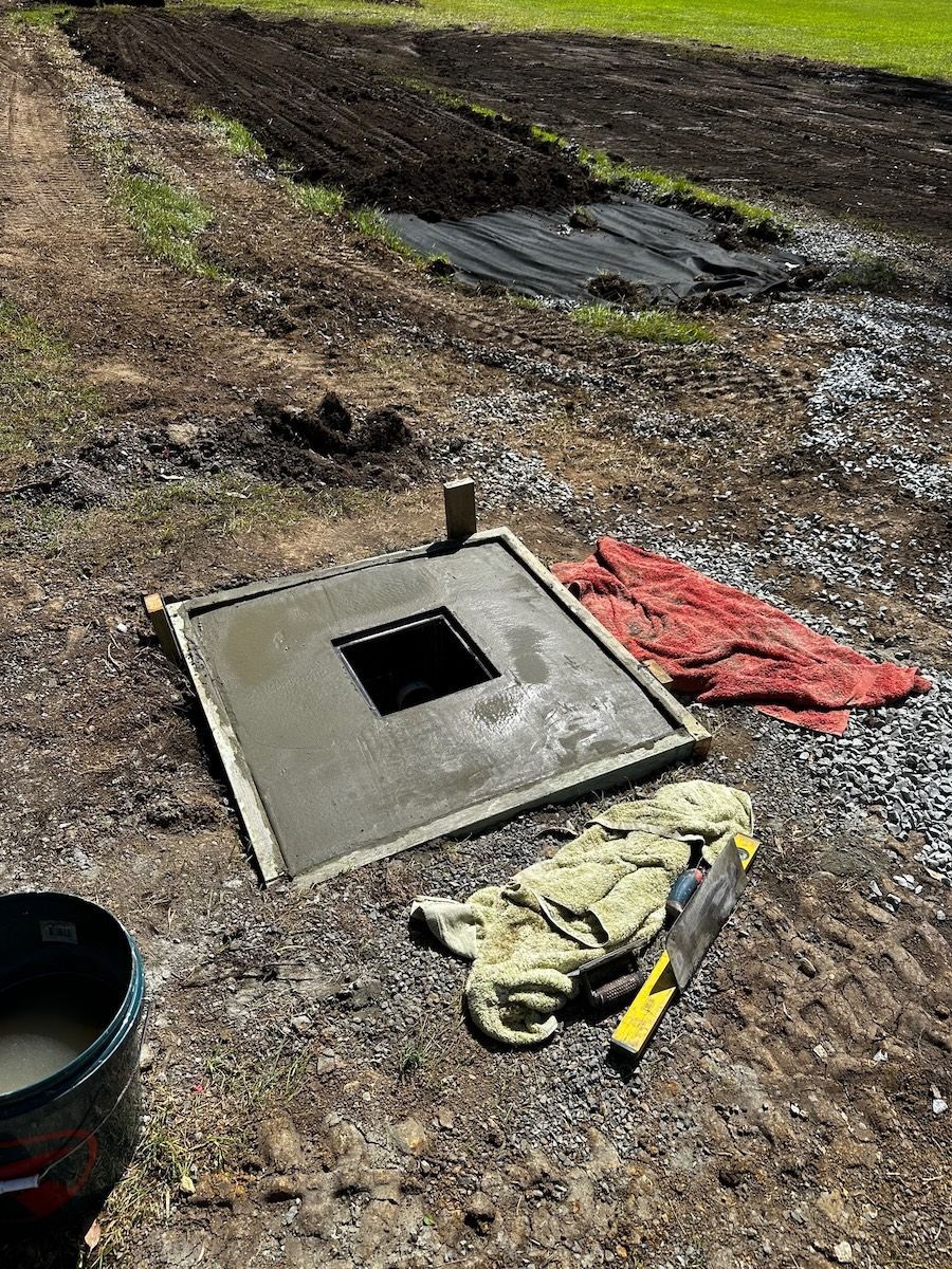 A Freshly Poured Concrete Square with A Central Square Opening, Set in An Outdoor Dirt Area Near Construction Tools — Port Macquarie Plumbing In Port Macquarie, NSW