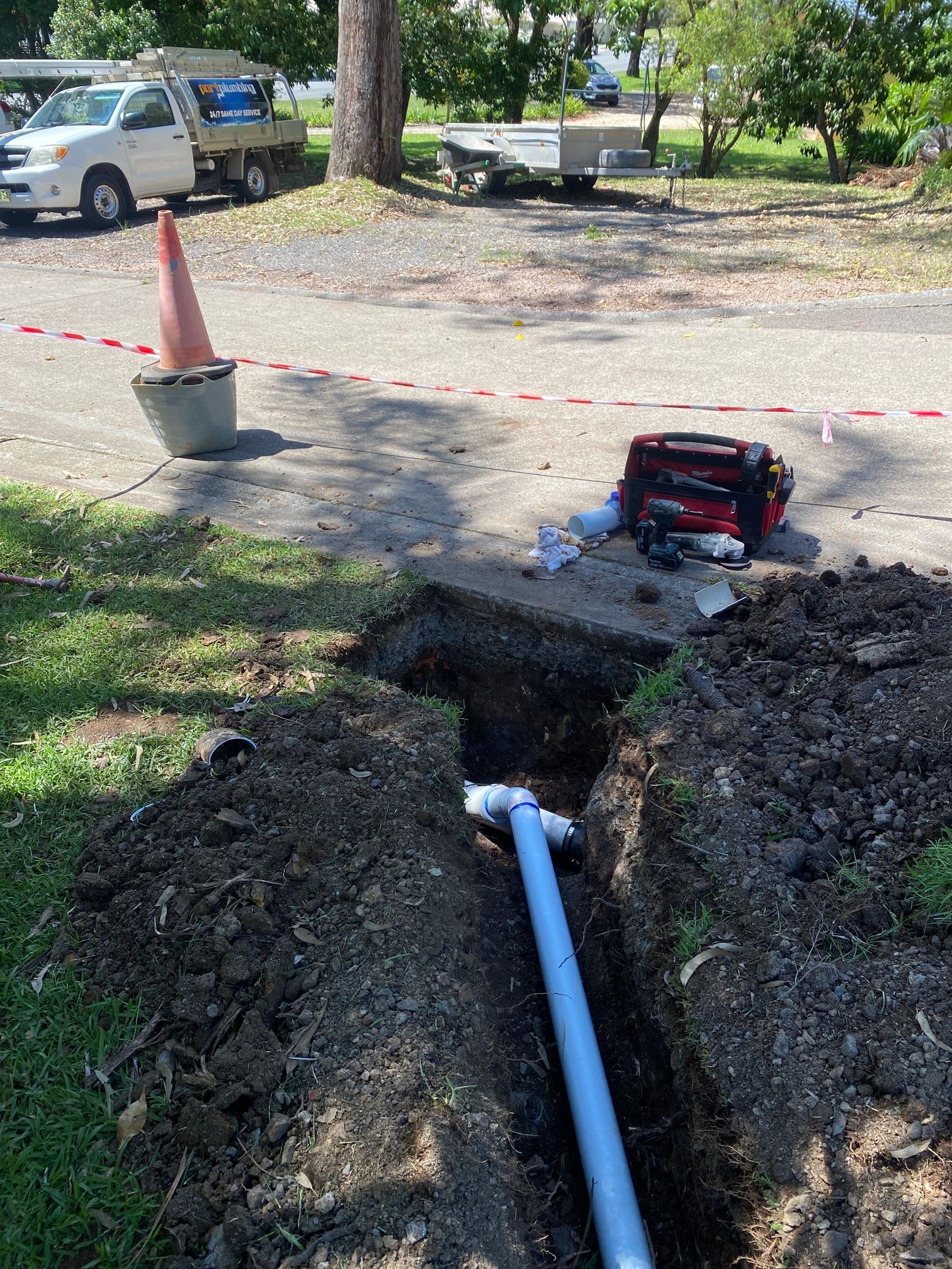 Open Trench with White Pipe and Utility Equipment Beside a Red Cone — Port Macquarie Plumbing In Port Macquarie, NSW