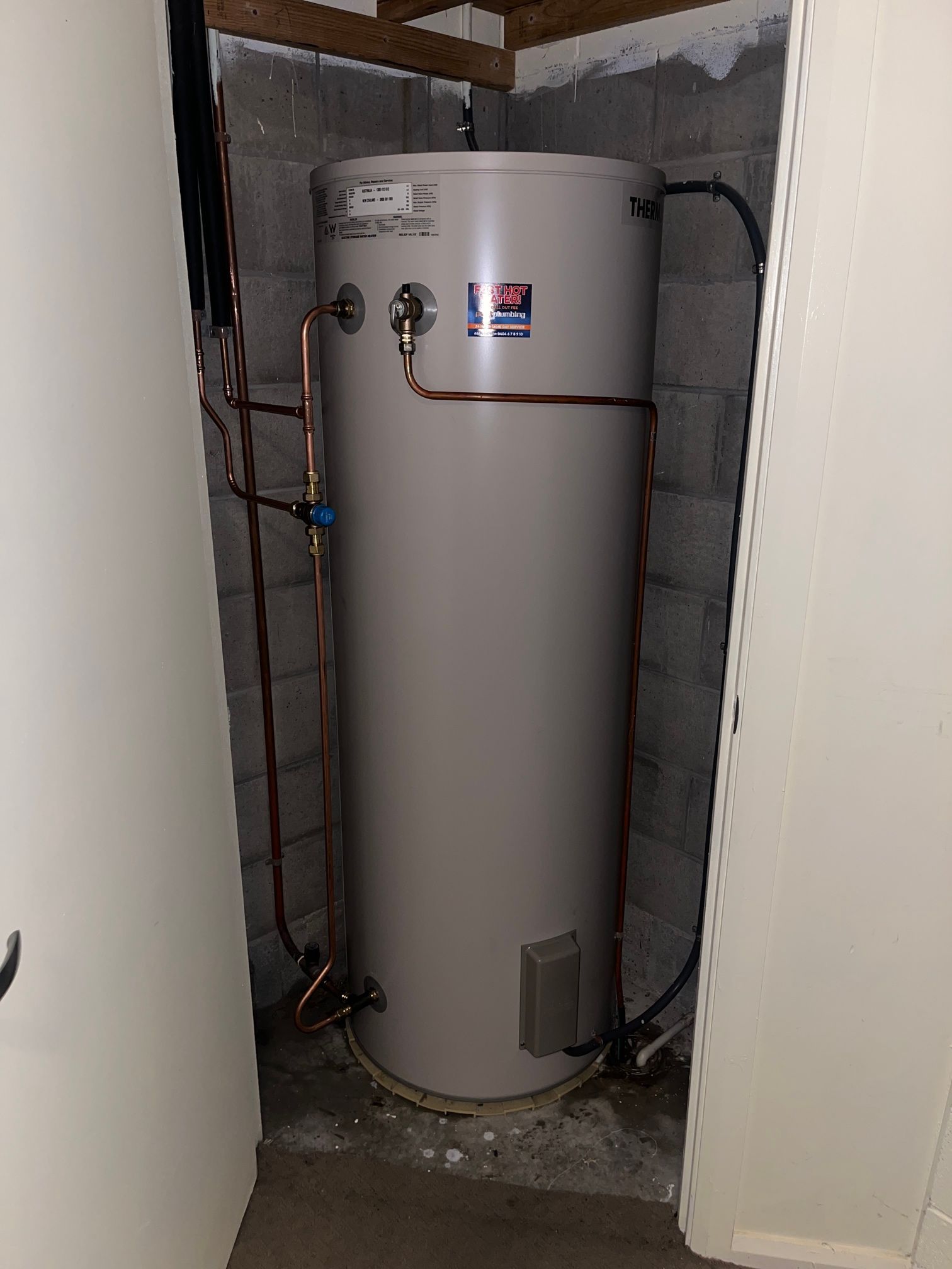 Tall Gray Water Heater in A Narrow Utility Closet with Visible Pipes and Valves — Port Macquarie Plumbing In Port Macquarie, NSW