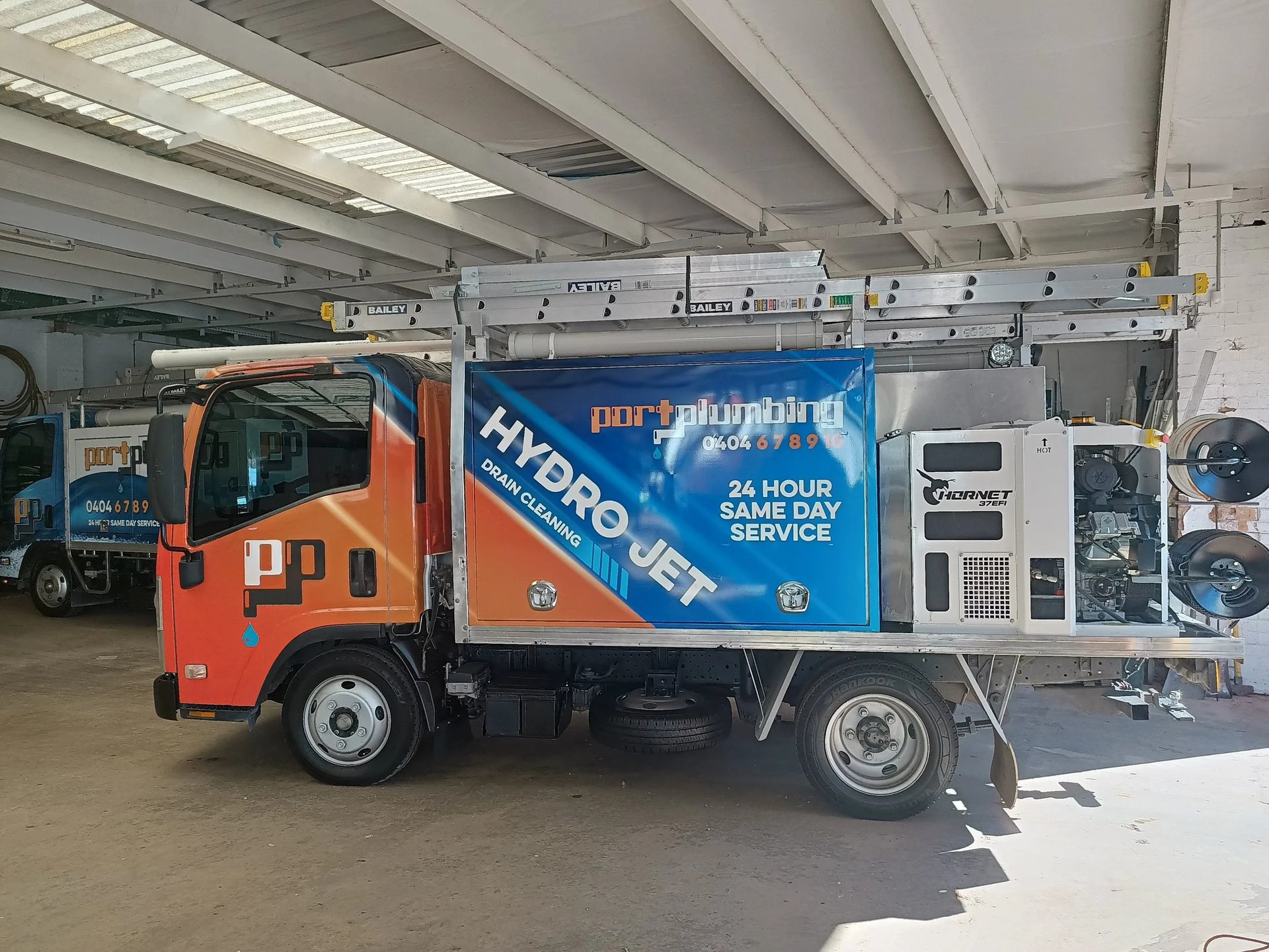 An Orange and Blue Plumbing Service Truck Parked Inside a Warehouse — Port Macquarie Plumbing In Port Macquarie, NSW