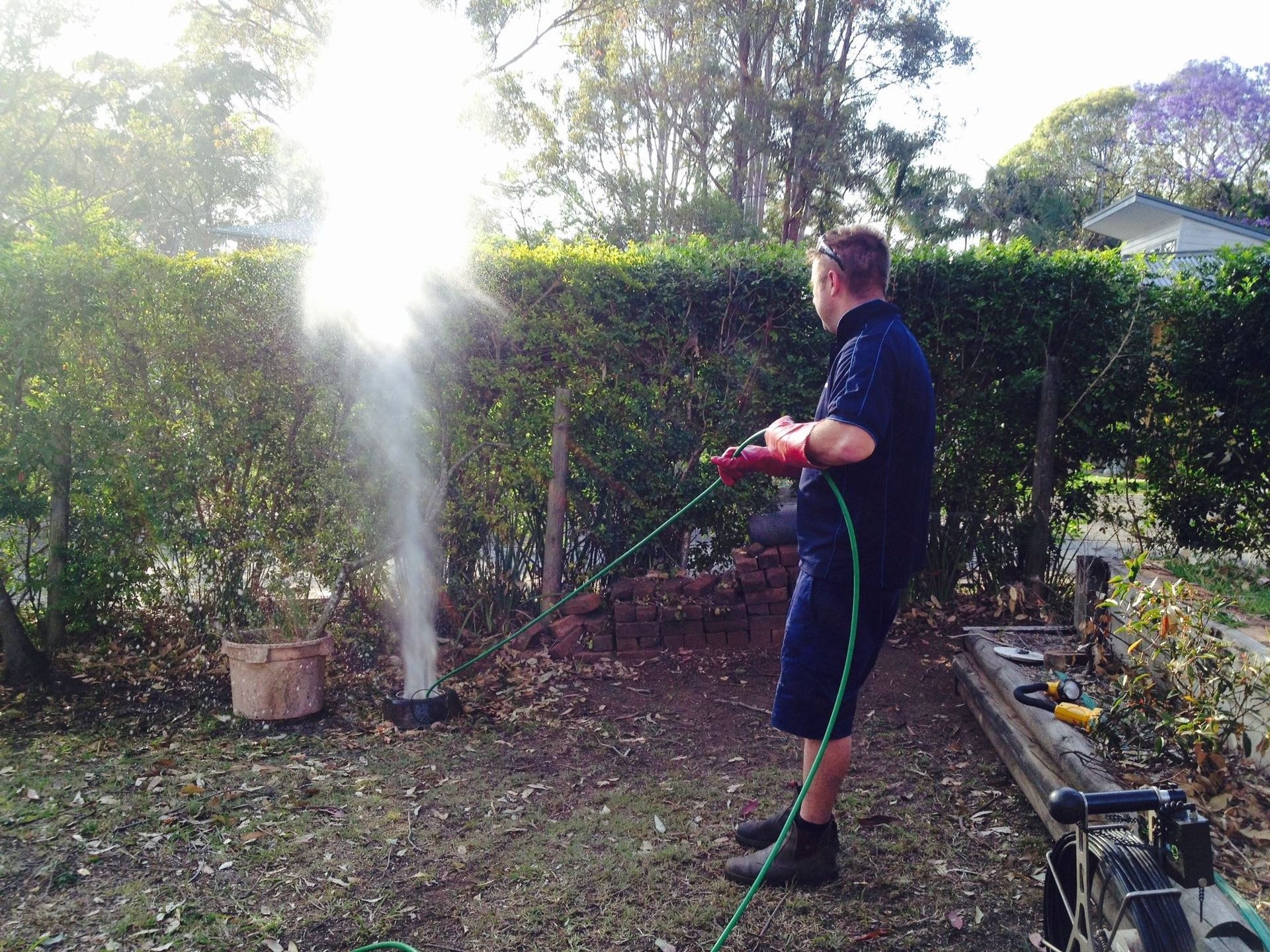 Person Pulling a Hose from A Whole in A Yard — Port Macquarie Plumbing In Port Macquarie, NSW