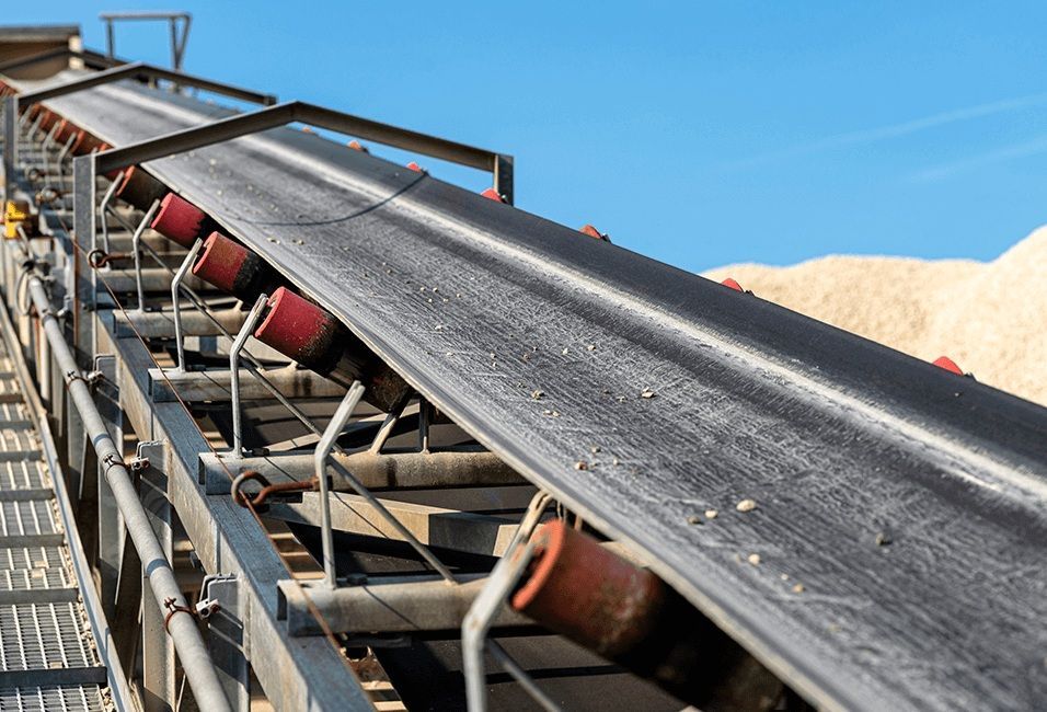 Conveyor belt carrying dark material at a mining or quarry site under a blue sky
