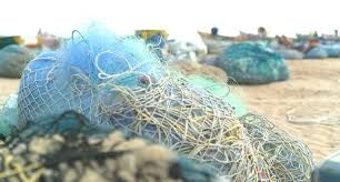 Blue fishing nets piled on a sandy beach with boats blurred in the background