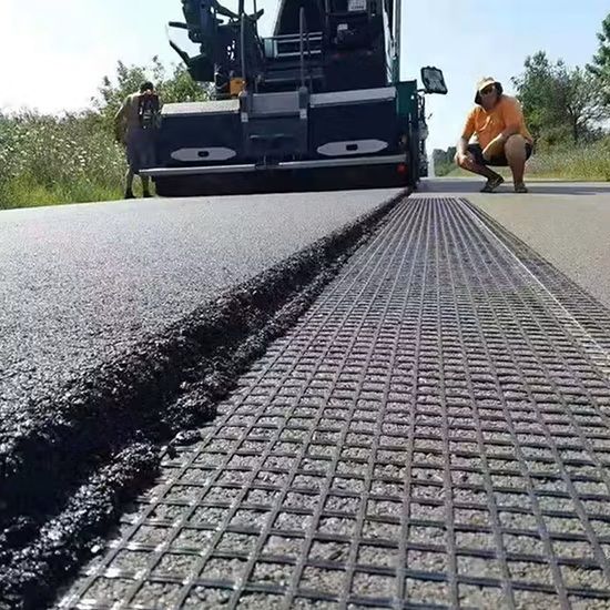 Road paving machine laying fresh asphalt beside a textured metal mat on a roadway