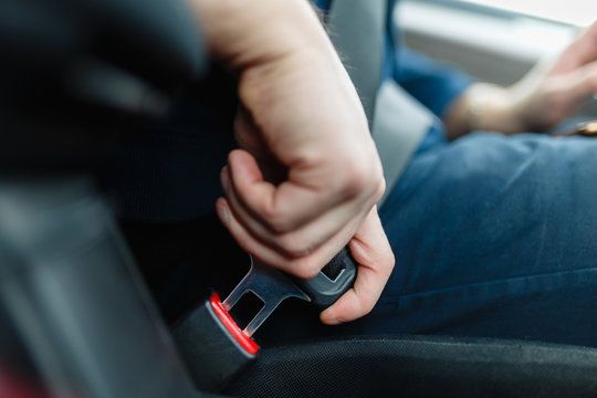 Hand gripping a car seatbelt buckle in a vehicle interior