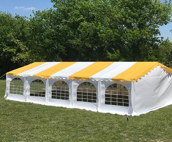 White and yellow striped event tent on a grassy lawn with trees in the background