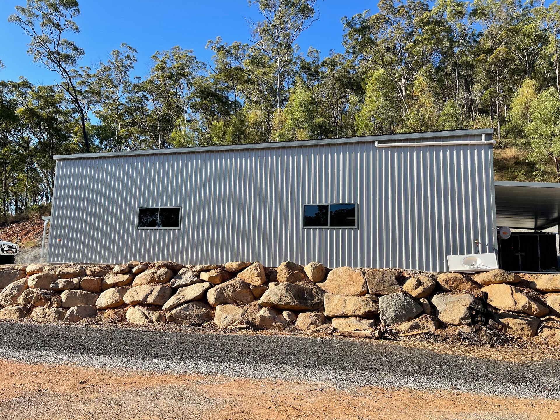 A Large Metal Building Is Sitting Next To A Rock Wall — AST Steel Constructions in Tannum Sands, QLD
