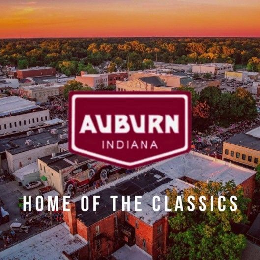 Aerial view of Auburn, Indiana at sunset with “Home of the Classics” text, representing local service area for Dead One Pest Control. Auburn, Indiana sign over aerial downtown at sunset with “Home of the Classics” text