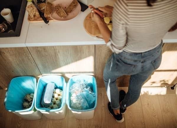 Person sorting trash into three recycling bins in a kitchen.