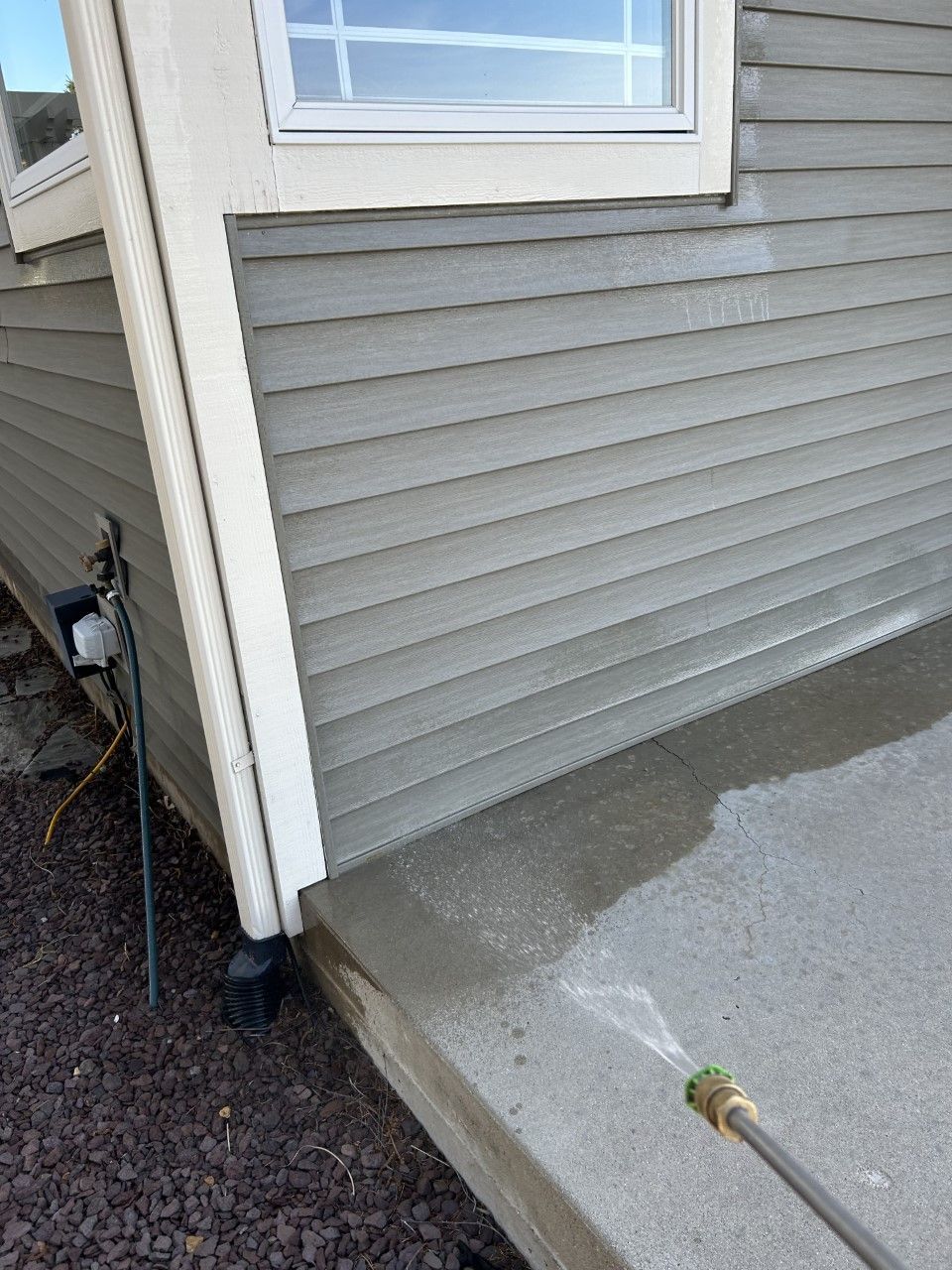 Power washing a house's gray siding next to a window and concrete step.