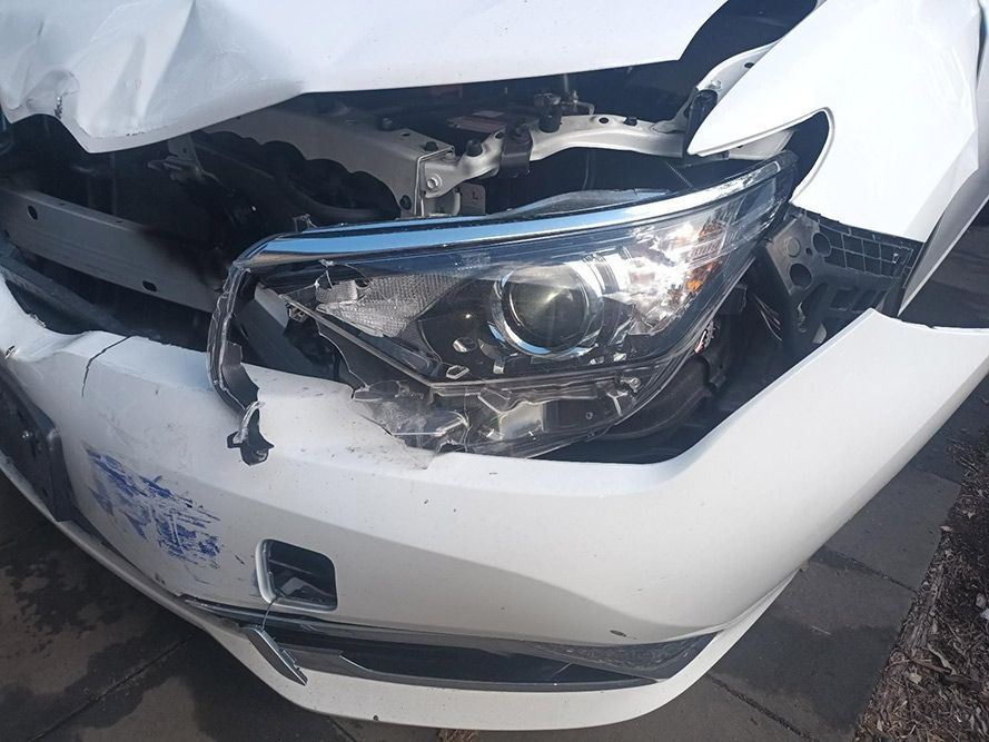 A White Car with a Broken Headlight is Parked on the Side of the Road — South West 4WD Wreckers In Brisbane, QLD