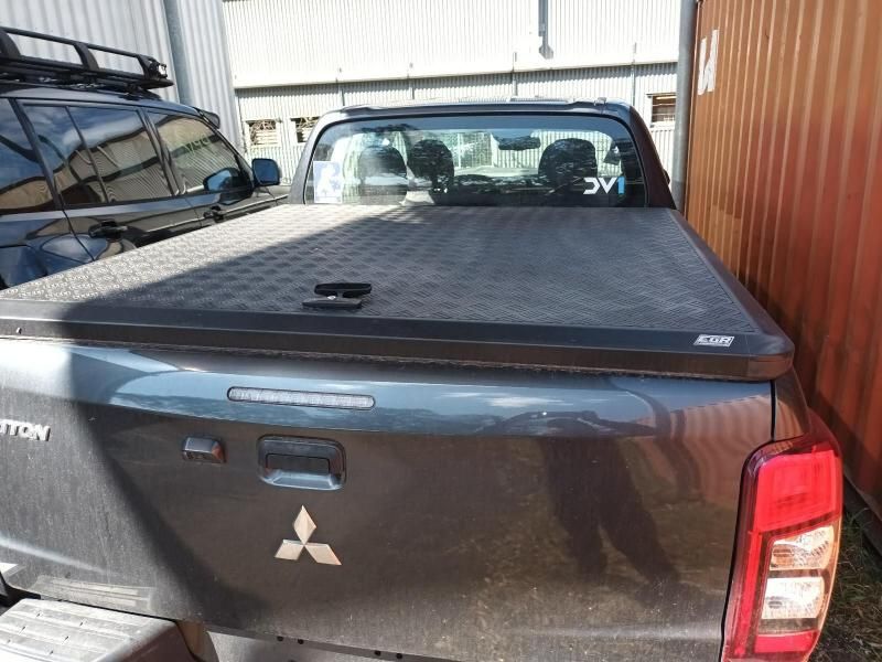 A Black Mitsubishi Truck With a Black Bed Cover is Parked in Front of a Building — South West 4WD Wreckers In Brisbane, QLD