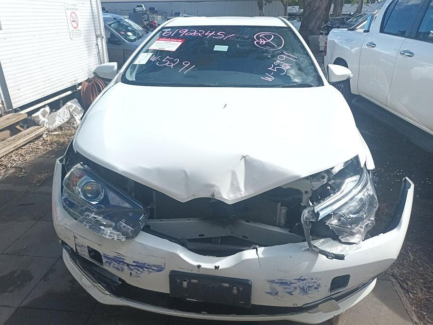 A White Car with a Damaged Front Bumper is Parked on the Side of the Road — South West 4WD Wreckers In Brisbane, QLD