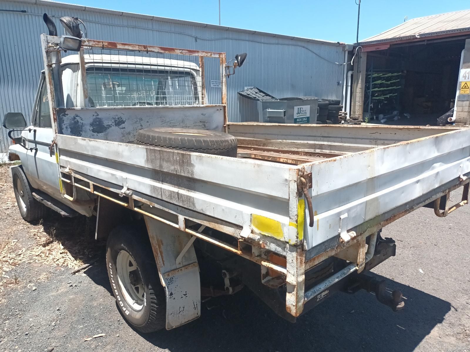 A White Truck with a Flat Bed is Parked in Front of a Building — South West 4WD Wreckers In Brisbane, QLD