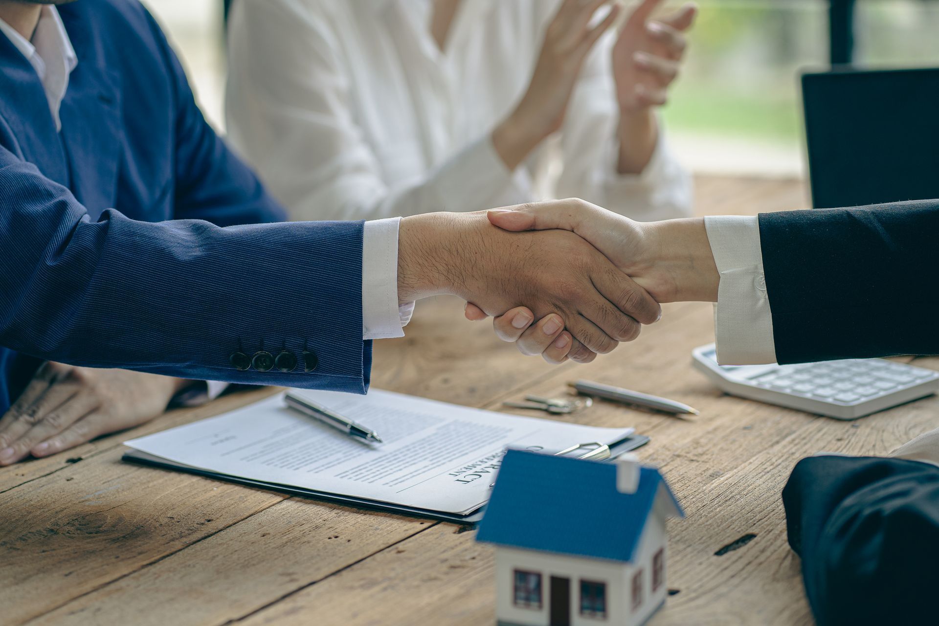 A man and a woman are shaking hands over a wooden table.