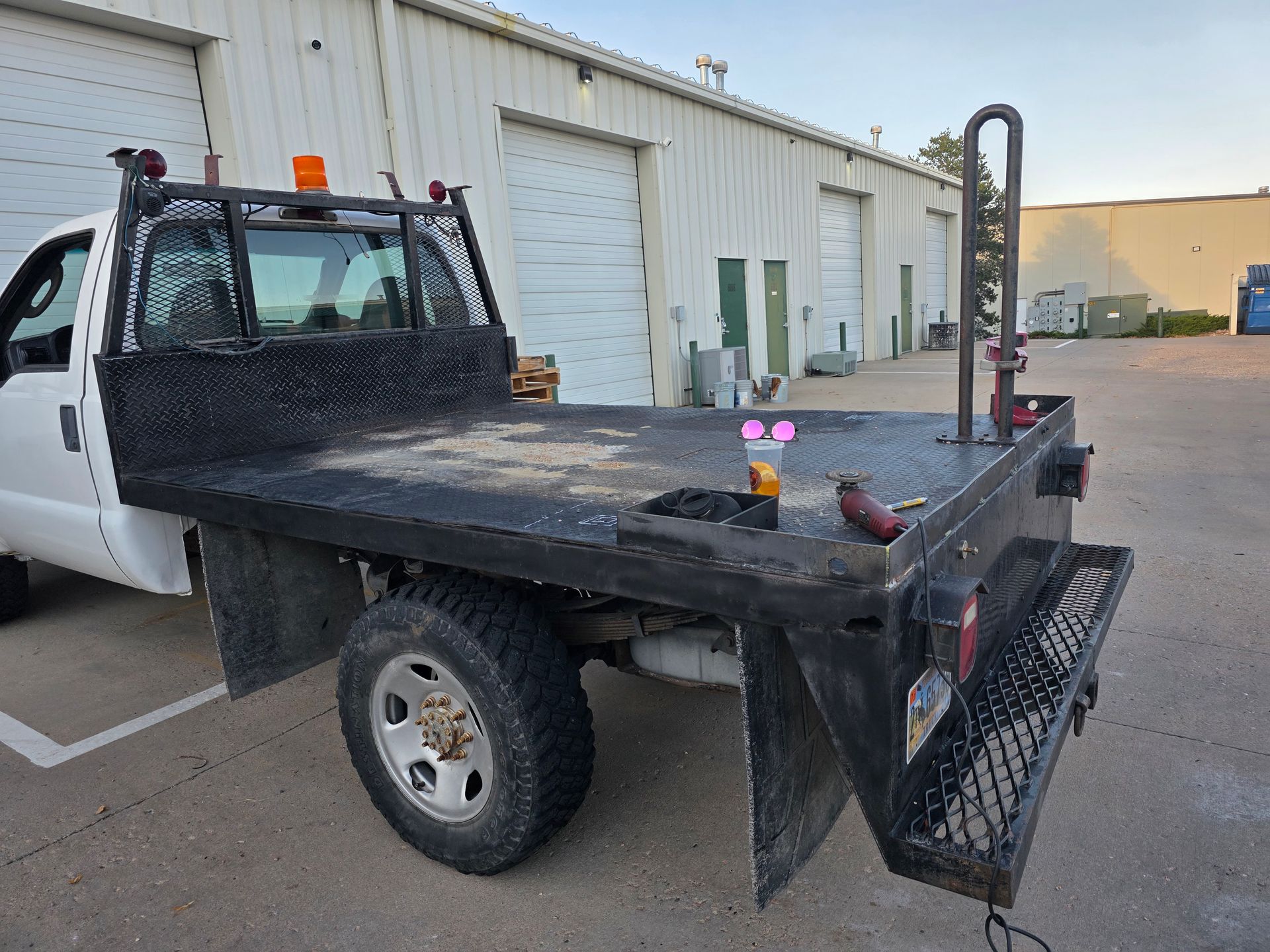 White flatbed truck parked in front of a building with overhead doors.